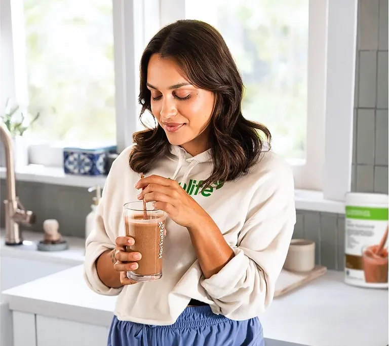 A woman enjoying a chocolate Formula 1 shake in her kitchen