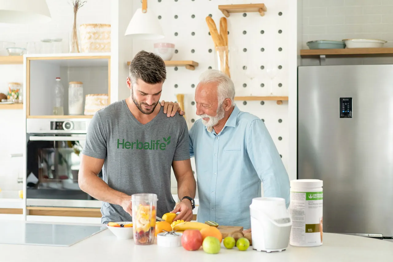 A father and son preparing a protein shake with fruit in a kitchen