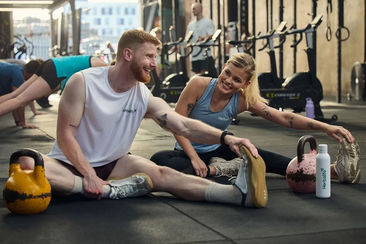 A man and a woman stretching on the gym floor after training